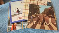 Seven vinyl album covers spread on floor including The Beatles' Abbey Road and Wha-Koo's plaid cover with eyes