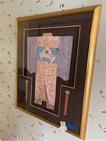 Photo showing the framed paper and ribbon kimono wall art hung on a floral wallpapered wall, captured from a slight angle.