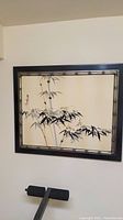 Full view of the bamboo wall art print hanging on a wall with visible bamboo stalk and leaves artwork and dark wood frame with bamboo-styled inner border.