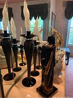 Photo showing three tall black candleholders with textured metal stems and imitation flames, arranged on a table with mirror反射。