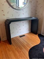 Black textured modern console or entry table positioned against a wallpapered wall with a mirror above it.