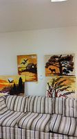 Four framed hooked yarn landscape panels arranged on and above striped sofa, showcasing diverse nature scenes with deer, birds, trees, and sunset colors.
