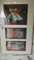 Photo shows framed artwork with mixed copper and patina elements arranged in abstract geometric shapes.