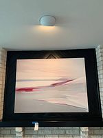 Front view of large signed abstract canvas wall art hanging above fireplace with black and white stone brick wall behind it.