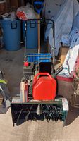 Front view showing snowblower housing, augers and attached shovel handle in background