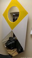 Front view of the plastic wall art mirror hanging on the wall showing the yellow diamond shape and round mirror.