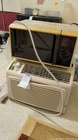 Photo of a vintage GE microwave sitting on top of a Kenmore window air conditioner, both beige/yellowed plastic, showing signs of use and dust.