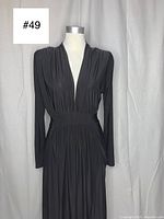 Front view of black floor length gown on mannequin showing deep V neckline, long sleeves, and gathered waistband.