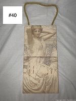 Front view of the hanging tile plaque with visible painted relief of a Grecian woman with her arms raised and detailed classical dress