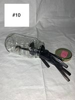 Clear glass mason jar with 11 hand carved horn spoons inside lying on white background. The open jar shows spoons with carved handles in natural horn colors.