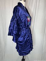 Side view of navy blue satin robe showing smooth shiny fabric, wide sleeves, front pocket and sash belt tied at waist.
