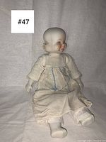 The full doll seated with fabric dress visible, head turned to the side showing the smooth porcelain head and fabric clothes.