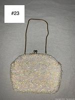 Top view of small oval purse with cream sequins and beads on fabric exterior, gold-tone metal frame and chain handle