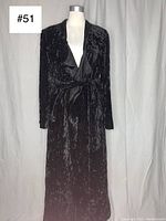 Front view of the black crushed velvet robe jacket on a mannequin, showing its length, fabric texture, and sash belt.