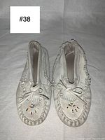 Front view of white suede moccasins showing beaded detail on toe and bow on vamp.