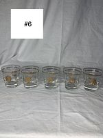 Front view of the five vintage lowball glasses arranged in a single line, showing gold pinwheel designs and gold rims.
