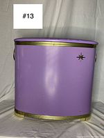 Front view of the purple hamper showing its curved shape, gold trim, and atomic starburst decoration on the side.