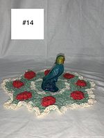 Photo showing vintage parrot Avon perfume bottle placed on hand crocheted rose doily with red roses and cream ruffled border.