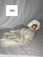 Full view of vintage Victorian style porcelain doll lying on its tummy, showing full outfit and bonnet.