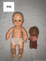 Photo showing two vintage rubber baby dolls: large light-skinned doll with molded hair and underwear, and smaller dark-skinned wearing clothes.