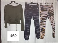 Photo of the three workout clothing items on hangers showing the patterns of the two leggings and the front of the green ruched crop shirt.