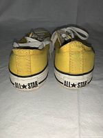 Rear view of yellow Converse sneakers showing the 'All Star' logos on the heel.