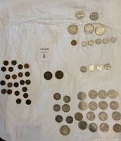 Top-down view of assorted Canadian coins laid on white fabric, showing silver dollars, 50 cent coins, quarters, nickels, and pennies, displaying condition variation.