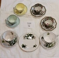All tea cups, saucers, and side plates arranged on a white cloth to show full set and matching designs