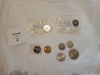 Photo showing the full assortment of 8 commemorative coins and tokens arranged on a white background, including Olympic coins, church token, Calgary Stampede, and Silver Jubilee coins.