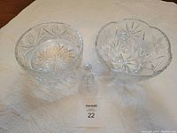 Wide shot of two round crystal bowls with cut star and floral patterns, accompanied by a clear crystal bell standing front and center on a white cloth.