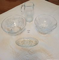 Photo of four glassware pieces: a serving bowl, pedestal bowl, candy dish, and water pitcher on white cloth