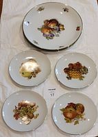 Six assorted decorative plates arranged on cloth background; four smaller Winterling plates with various fruit designs and two larger Bavaria plates with fruit designs and gold rims.