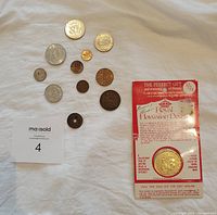 Photo showing twelve assorted foreign coins arranged on fabric with a label and the Royal Hawaiian Dollar replica card adjacent.
