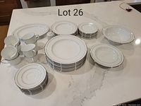 Full Noritake Stoneleigh china set arranged on white counter showing all plates, bowls, cups, saucers, pepper shaker, and serving platter with silver trim.