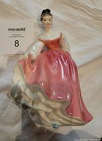 Royal Doulton Fair Lady porcelain figurine showing woman in pink dress lying on fabric background, with MaxSold label.