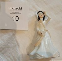 Front and partial side view of the Royal Doulton Helen figurine, showing woman in white flowing dress holding a tan feather.