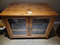 Full front view of wood TV cabinet with glass doors and metal knobs.