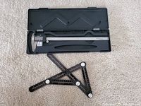 Digital caliper inside black plastic case on carpet, different angle showing case and tool fit.