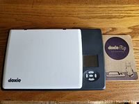 Closed Doxie Flip scanner with white lid, black base, display screen, buttons, and manual on wooden surface.