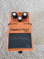 Top-down view of orange Boss DS-1 distortion pedal showing tone, distortion, and level control knobs, power indicator LED, input and output labels, and branding.
