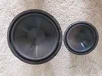 Front view showing two black cone speakers, one larger and one smaller, placed side by side on carpeted floor.