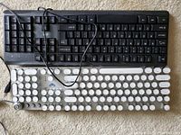 Top view photo showing two USB keyboards: one black standard keyboard, one white round-key styled mechanical keyboard