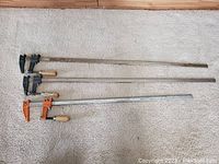 Top view of three metal carpentry clamps laid out horizontally showing their full length and handles.