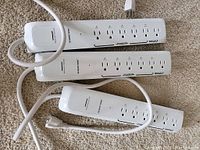 Three white CE Smart Home WiFi power bars laid on carpet, each with 6 outlets and attached cords visible.