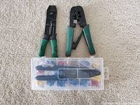 Two green-handled wire strippers and cutters with a plastic container with assorted electrical connectors on a beige carpet
