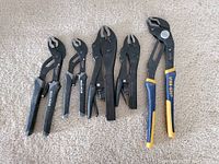 Set of six locking and groove joint pliers arranged on carpet, showing different brands and sizes