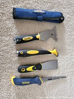 Drywall and paint tools including saws and scrapers arranged on carpet showing brand and handle details