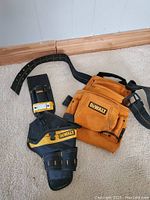 Full view of the tan leather Dewalt tool belt laid flat on carpet, showing multiple pockets and black straps.