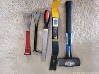 Full view of four pry bars and a sledgehammer lying on carpeted floor.