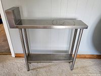 Front and side view of the Quest Metal Works stainless steel kitchen service table showing tubular legs, lower shelf and backsplash